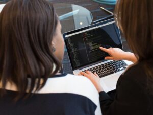 Two women working together on software programming indoors, focusing on code.