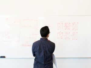 Man standing at a whiteboard planning UX design concepts in a modern office setting.