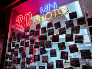 Vintage photo shop with neon sign displaying 30 min photo service surrounded by hanging polaroids.