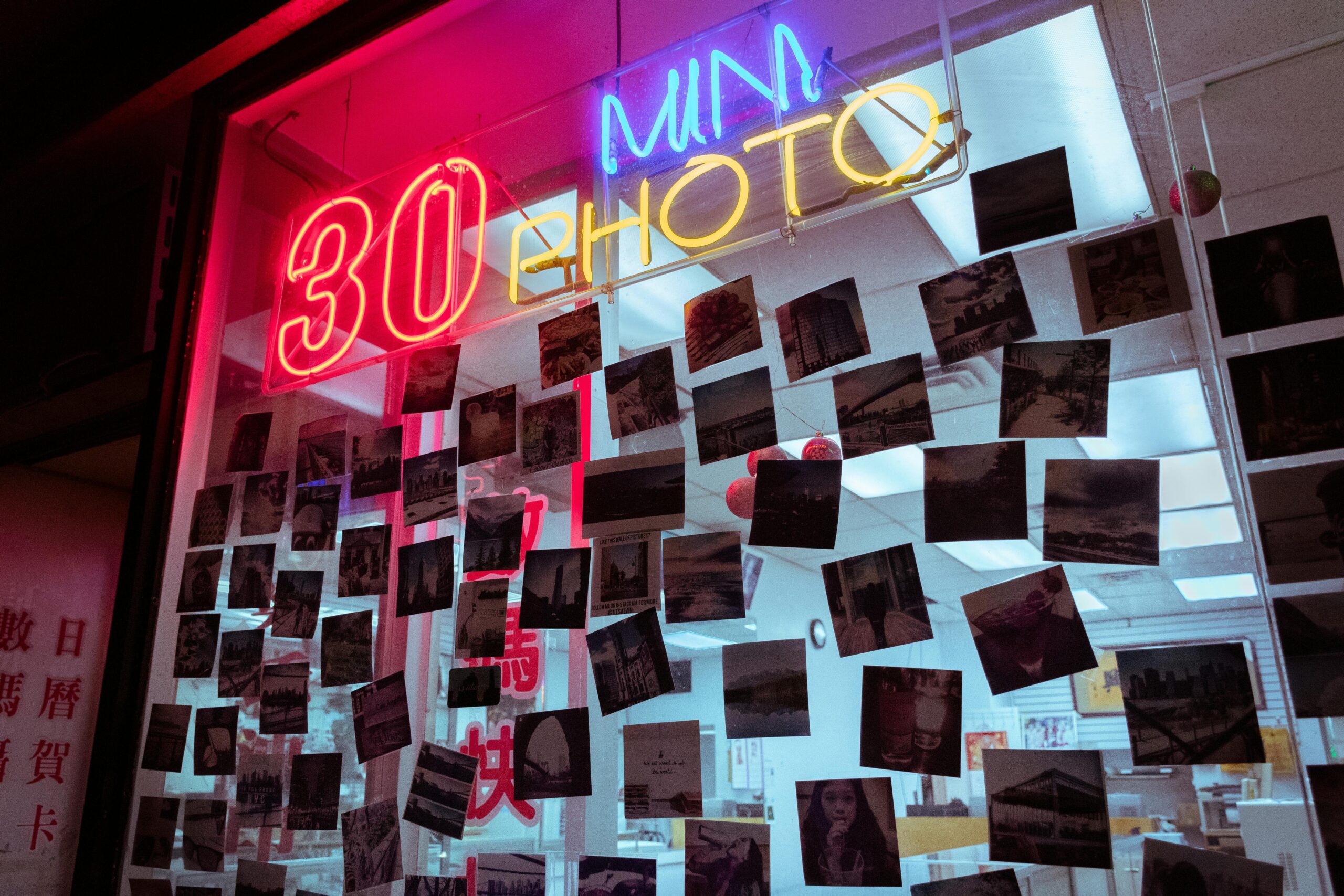 Vintage photo shop with neon sign displaying 30 min photo service surrounded by hanging polaroids.