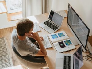 Top view of young programmer working on multiple laptops in a modern office setting.