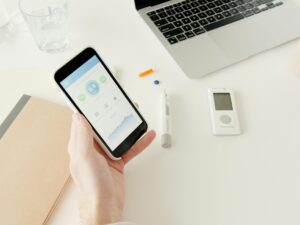 A person checks glucose levels on a smartphone app next to diabetes monitoring equipment.