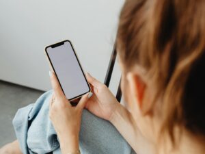 A woman holds a smartphone with a blank screen indoors, offering a mockup opportunity.